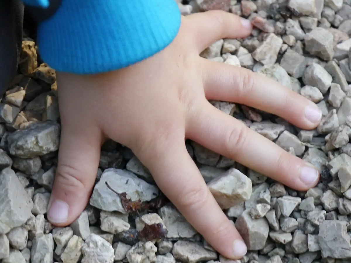 Eine Kinderhand berührt den Kiesboden