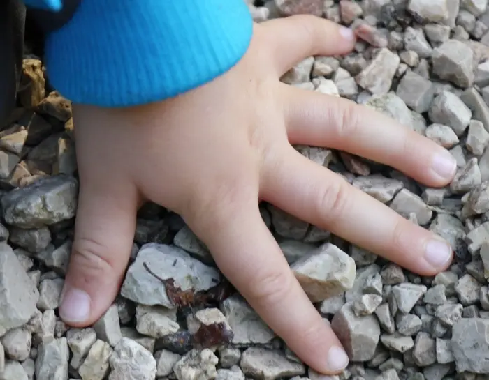 Eine Kinderhand berührt den Kiesboden